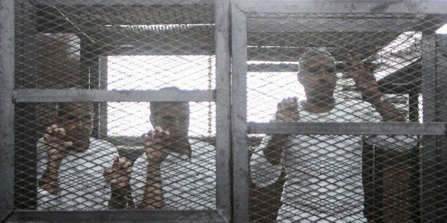 Defendents who are in custody stand in the accused cells during the trial of 20 individuals, including five Al-Jazeera journalists, for allegedly defaming the country and ties to the blacklisted Muslim Brotherhood on May 3, 2014 in the police institute near Cairo's Turah prison. Peter Greste (L), an Australian journalist with satellite news channel Al-Jazeera on trial described his ordeal as a 'massive injustice', after spending more than four months in jail. AFP PHOTO / MOHAMED EL-SHAHED (Photo credit should read MOHAMED EL-SHAHED/AFP/Getty Images)
