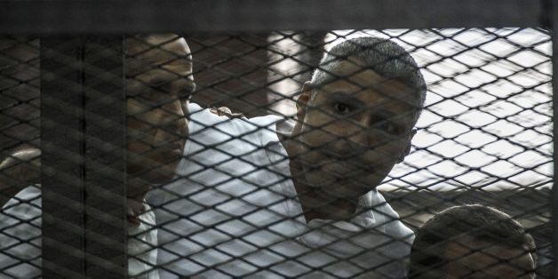 Al-Jazeera news channel's Australian journalist Peter Greste (L) and his colleagues, Egyptian-Canadian Mohamed Fadel Fahmy (C) and Egyptian Baher Mohamed , listen to the verdict inside the defendants cage during their trial for allegedly supporting the Muslim Brotherhood on June 23, 2014 at the police institute near Cairo's Tora prison. The Egyptian court sentenced the three Al-Jazeera journalists to jail terms ranging from seven to 10 years after accusing them of aiding the blacklisted Brotherhood. Since the army ousted Islamist president Mohamed Morsi in July 2013, the authorities have been incensed by the Qatari network's coverage of their deadly crackdown on his supporters. AFP PHOTO / KHALED DESOUKI (Photo credit should read KHALED DESOUKI/AFP/Getty Images)