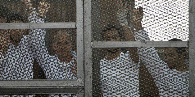Australian journalist Peter Greste (2ndL) of Al-Jazeera and his colleagues stand inside the defendants cage during their trial for allegedly supporting the Muslim Brotherhood at Cairo's Tora prison on March 5, 2014. The high-profile case that sparked a global outcry over muzzling of the press is seen as a test of the military-installed government's tolerance of independent media, with activists fearing a return to autocracy three years after the Arab Spring uprising that toppled Hosni Mubarak. AFP PHOTO / KHALED DESOUKI (Photo credit should read KHALED DESOUKI/AFP/Getty Images)