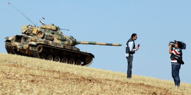 A journalist makes a report backdropped by a Turkish tank holding its position on a hilltop on the outskirts of Suruc, at the Turkey-Syria border, overlooking Kobani in Syria where fighting had ben intensified between Syrian Kurds and the militants of Islamic State, Monday, Oct. 6, 2014. Kobani, also known as Ayn Arab and its surrounding areas have been under attack since mid-September, with militants capturing dozens of nearby Kurdish villages. (AP Photo/Lefteris Pitarakis)