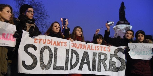 Journalism students hold a banner reading in French: 'Journalism students : Solidarity' as they raise pens during a gathering at the Place de la Republique (Republic square) in Paris, on January 7, 2015, following an attack by unknown gunmen on the offices of the satirical weekly, Charlie Hebdo. France's Muslim leadership sharply condemned the shooting at the Paris satirical weekly that left at least 12 people dead as a 'barbaric' attack and an assault on press freedom and democracy. AFP PHOTO / DOMINIQUE FAGET (Photo credit should read DOMINIQUE FAGET/AFP/Getty Images)