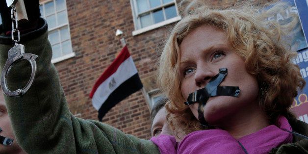 A journalist, with black tape over the mouth to illustrate the silencing of free speech and journalists, holds up a placard and a pair of handcuffs as she demonstrates across the street from the Egyptian Embassy to mark a year since the detention of Al-Jazeera English journalists in Egypt, central London, Monday, Dec. 29, 2014. The unprecedented arrest and prosecution of Australian Peter Greste, Egyptian-Canadian Mohammed Fahmy and Egyptian Baher Mohammed sent a chill through the media in Egypt. They were detained in a raid on suspicion of helping the Muslim Brotherhood, which the government later declared a terrorist organization, and were sentenced to between seven and 10 years in prison in a trial that most observers called a politicized sham that lacked any evidence to incriminate the journalists of anything beyond doing their job. (AP Photo/Lefteris Pitarakis)
