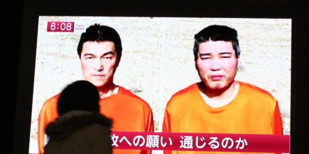 A passer-by watches a TV news program reporting two Japanese hostages, Kenji Goto, left, and Haruna Yukawa, held by the Islam