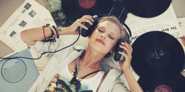 A young woman listening to music while lying on her back and surrounded by records