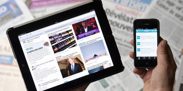 TO GO WITH AFP STORY BY TUPAC POINTU A man holds a tablet and a smartphone showing a news website and a Twitter news thread in front of world newspapers on September 12, 2013 in Paris. AFP PHOTO / LIONEL BONAVENTURE (Photo credit should read LIONEL BONAVENTURE/AFP/Getty Images)