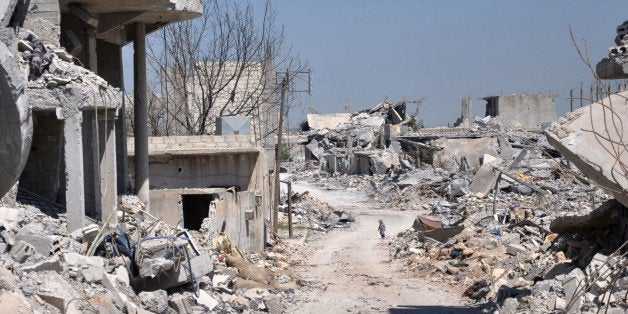 In this picture taken on Saturday, April 18, 2015, a Kurdish boy, center background, walks between buildings that were destroyed during the battle between the U.S. backed Kurdish forces and the Islamic State fighters, in Kobani, north Syria. The Kurdish town on the Turkish-Syrian border is still a haunting, apocalyptic vista of hollowed out facades and streets littered with unexploded ordnance - a testimony to the massive price that came with the victory over IS. (AP Photo/Mehmet Shakir)