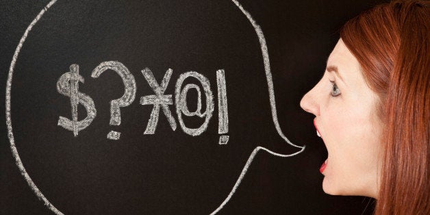 A woman stands by a chalk drawn talk bubble with swear symbols in it.