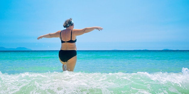 mature woman in swimwear at the sea. Overweight woman in swimsuit comes in water in time of surf, rear view