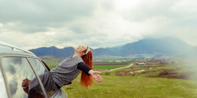 happy woman sitting on car open window with arms raised and feeling free.