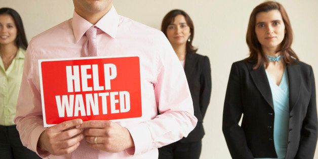 Portrait of three businesswomen standing with a businessman holding a help wanted signboard