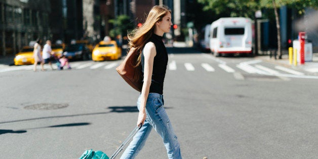 USA, New York City, young woman with rolling suitcase crossing a street