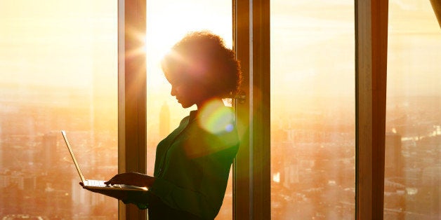 Businesswoman on laptop at window in morning sun