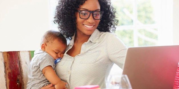 Mother With Baby Working In Office At Home Looking At Laptop