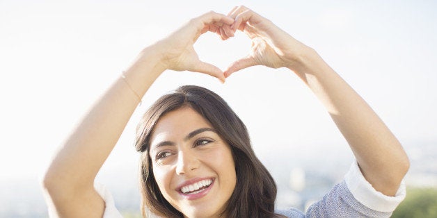 Woman making heart-shape with hands outdoors