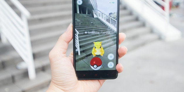 Penang, Malaysia - August 13, 2016 : Close of a man holding a smartphone with his left hand playing Pokemon Go game on the stair. On the screen of the smartphone is a Pokemon character called 'Sandschrew'.