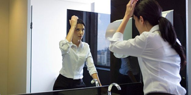 Businesswoman looking in mirror, adjusting hair