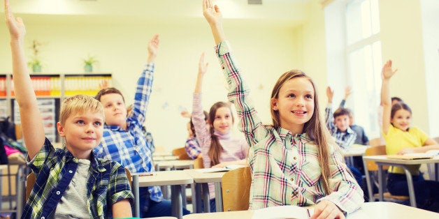 education, elementary school, learning and people concept - group of school kids with notebooks sitting in classroom and raising hands