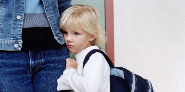 Girl (4-6) with backpack clinging on to mother