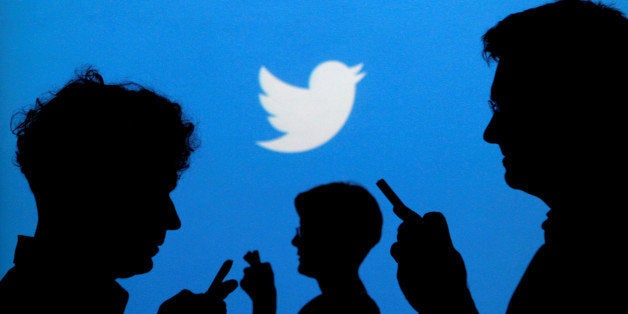 FILE PHOTO -- People holding mobile phones are silhouetted against a backdrop projected with the Twitter logo in this illust