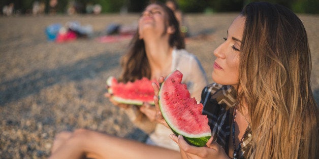 Girlfriends laughing and eating watermelon on the beach. Sunset