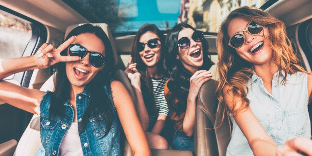 Four beautiful young cheerful women looking happy and playful while sitting in car