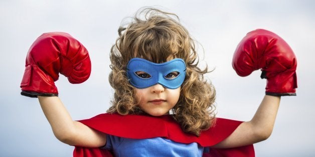 Superhero kid wearing boxing gloves against blue sky background. Girl power and feminism concept