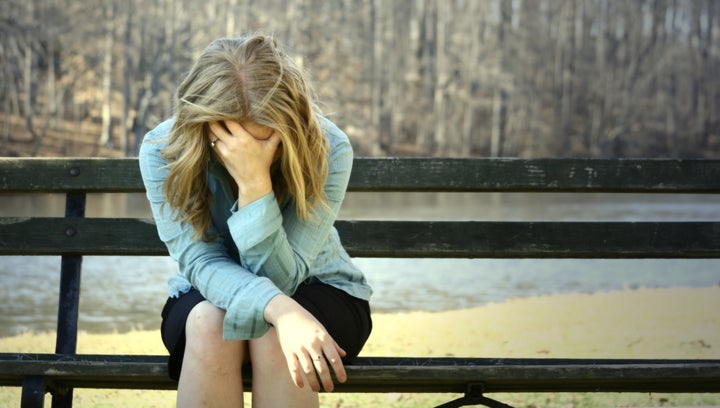 very sad blonde girl holding her head on a bench