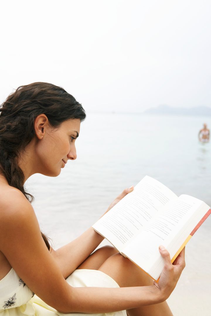 Young woman on beach, reading book
