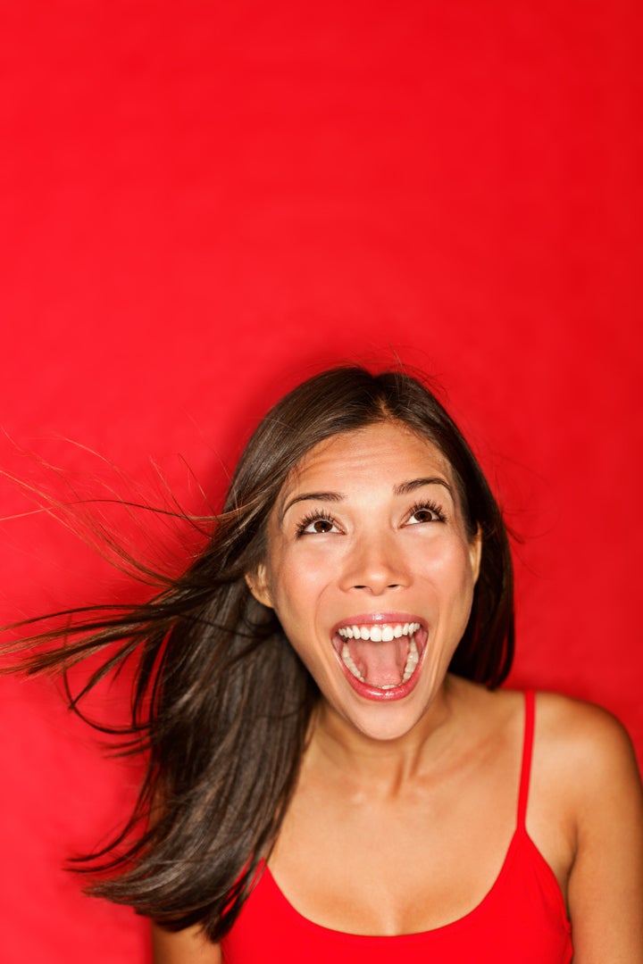 surprised screaming woman looking up at copy space on red background. Beautiful young shocked mixed race Caucasian / Asian female model amazed.