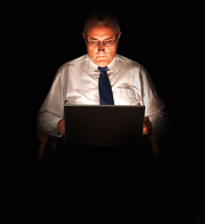 Old business man working on laptop in the dark