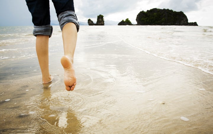 A young woman walks alone on a beach, just her feet and legs showing