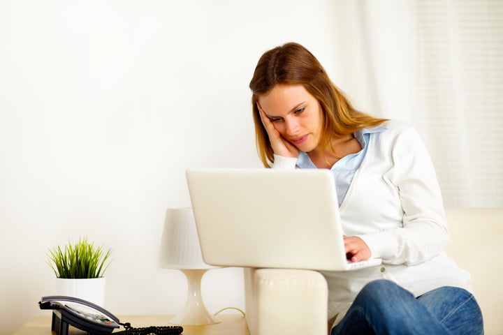 Portrait of a young boring woman working on laptop at home