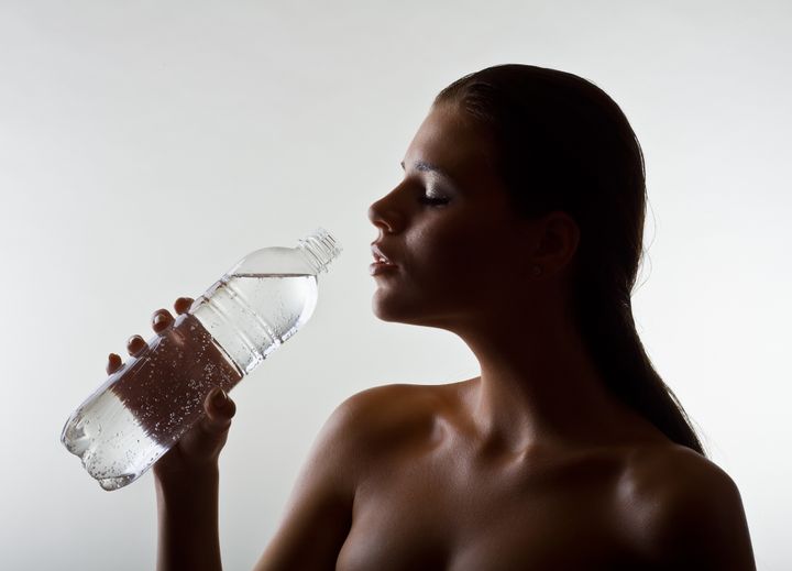 Wet a beautiful woman holding a water bottle, on light background