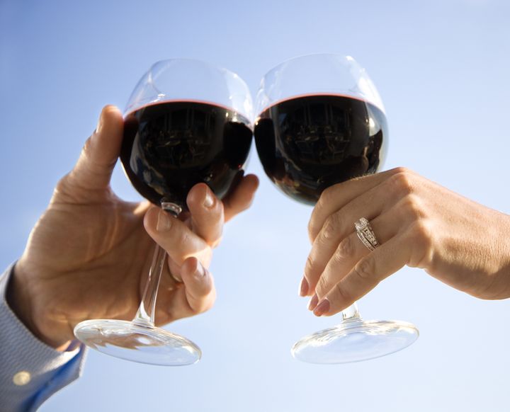 A married couple's hands toasting with red wine. Horizontal shot.