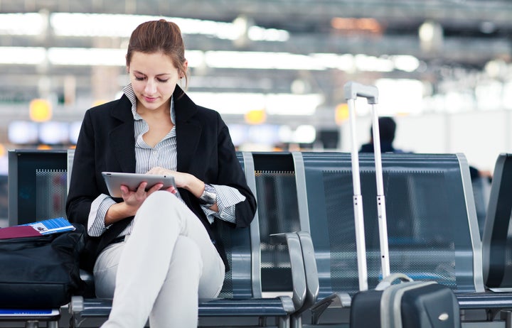 Young female passenger at the airport, using her tablet computer while waiting for her flight (color toned image)