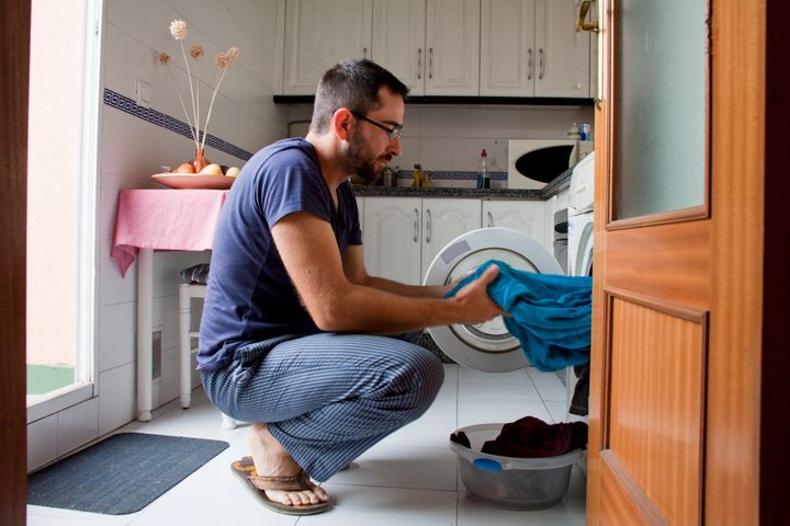 Close-up of man wearing blue pijama pulling towel from washing machine in kitchen.