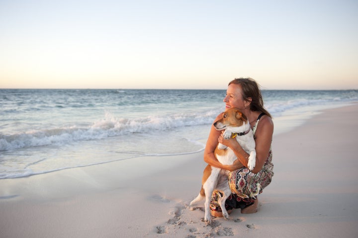 Happy looking mature woman is enjoying a sunset at the beach with her pet dog, with ocean and twilight sky as background and copy space.