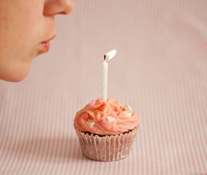 Woman blowing a candle on a pink cupcake