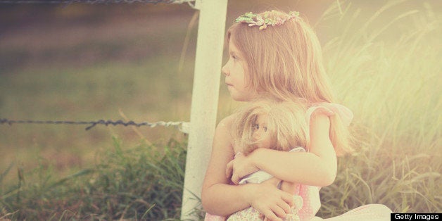 Little girl in a fancy dress, setting by a fence, holding a doll.