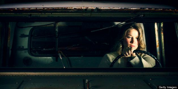 A beautiful, pensive woman in a broken down truck. Rifles in the back window.