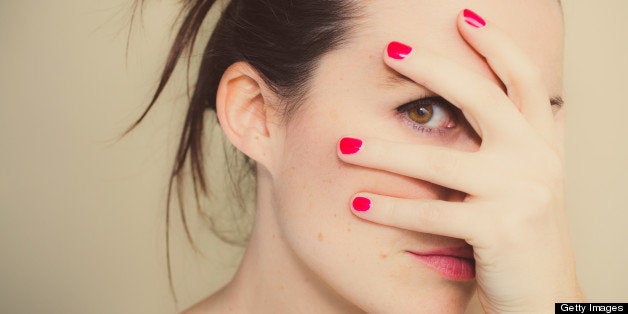 Close-up portrait. Girl covering her face with one hand and looking between her fingers. One brown eye and gathered hair.