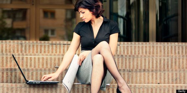 Gorgeous busy lady with sexy legs working outdoors at her laptop seating in front of a library