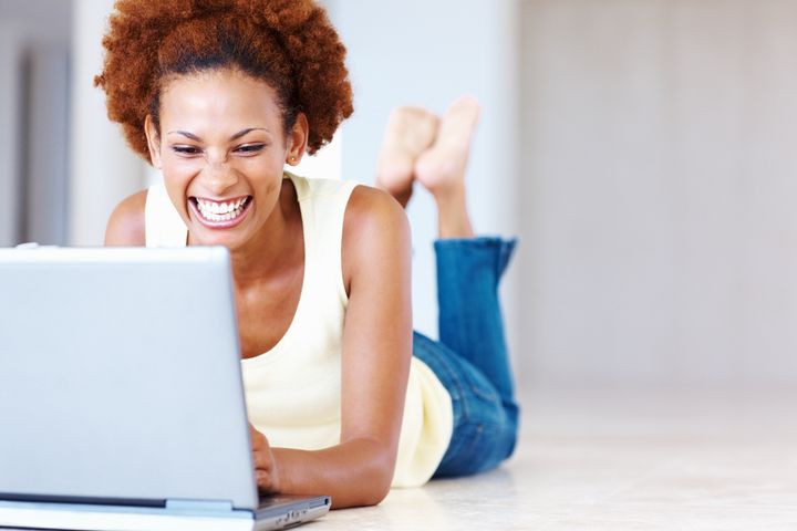 Happy African American woman lying on floor with laptop at home