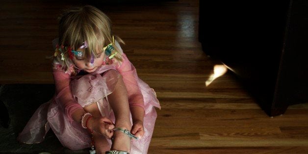 Toddler playing dress up; pink princess with silver shoes and barrettes in her hair. Little girl buckling her own shoe.