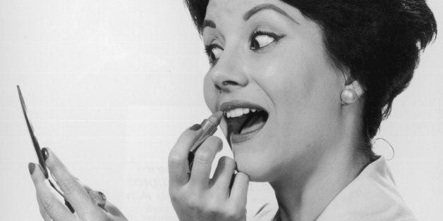 circa 1955: A portrait of a woman applying lipstick while looking in a compact mirror. (Photo by Lambert/Getty Images)