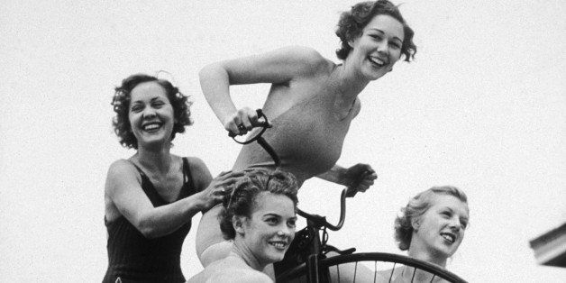 Full-length image of four young women wearing bathing suits posing on and around an old-fashioned penny farthing bicycle outdoors, 1930s. (Photo by Hulton Archive/Getty Images)