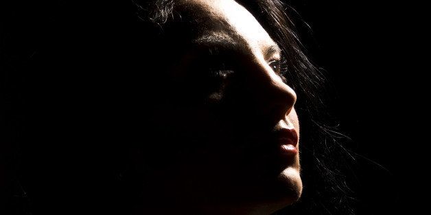 Portrait of beautiful brunette woman looking away in darkness with soft light on her face