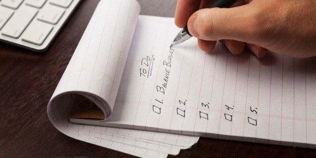 Closeup of a person writing out a to do list with finances as a first priority.