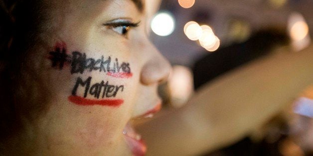 A message reading "Black Lives Matter" is written across the cheek of Samaria Muhammad as she chants with fellow protesters i