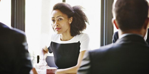 Businesswoman sitting at table in restaurant listening to colleagues in meeting